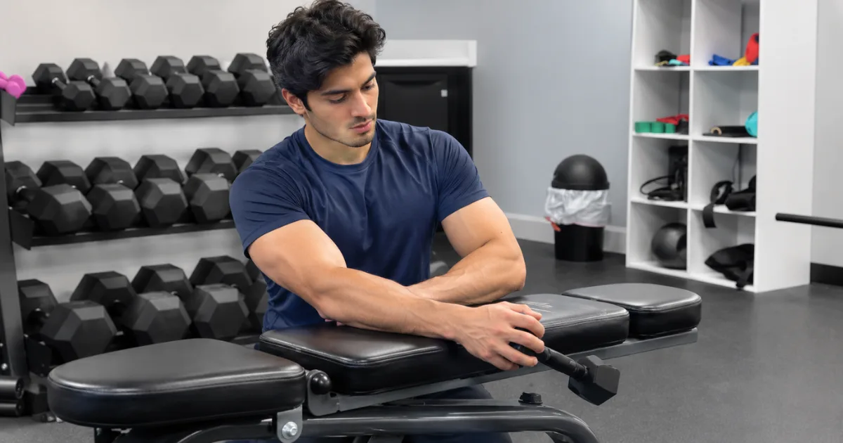 Athlete performing light dumbbell forearm supination exercise on a gym bench.
